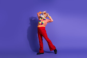 Mature man in eccentric retro outfit dancing on purple background showing funky style with colorful...