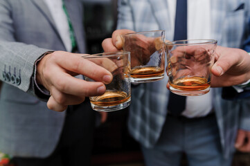 Three well-dressed men clinking rocks glasses filled with amber liquid, likely whiskey, celebrating a joyful occasion with camaraderie.