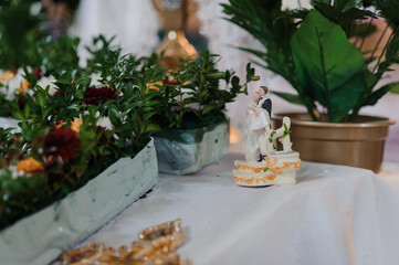 Wedding cake topper figurine of a couple with a dog, set among lush greenery and floral arrangements on a white tablecloth