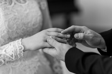 A tender moment captured in black and white, showing a groom placing a wedding band on the bride's...