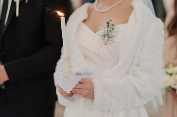 Close-up of wedding ceremony moment showing a bride holding a lit candle while exchanging vows,...