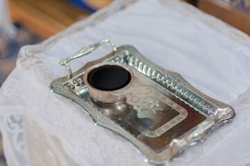 Silver tray with a small cup of dark liquid rests on a patterned white cloth with decorative...