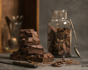 Stack of dark chocolate pieces and a jar on a rustic table