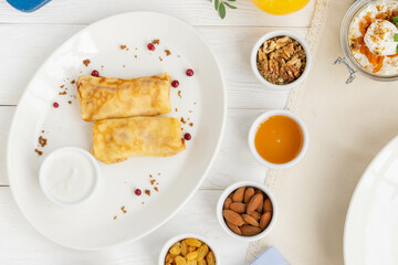 Golden crepes with assorted nuts, honey, and yogurt on a white plate