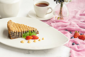 Slice of poppy seed cake with strawberries and tea on elegant white plate