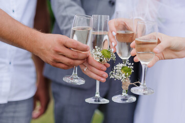 Celebrating Wedding Day: A joyful moment of four hands clinking champagne glasses adorned with delicate floral boutonnieres during a wedding toast