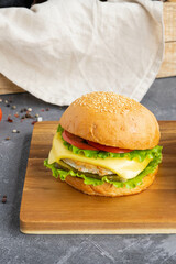 Delicious chicken burger with cheese and fresh vegetables on wooden board