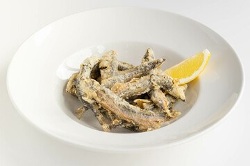 Bowl of crispy fried anchovies with lemon wedge on white plate