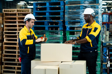 Teamwork between warehouse workers sealing cardboard boxes using tape dispenser while preparing for shipment in logistics warehouse, including african adult male and caucasian adult male staff