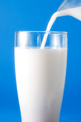 Fresh Milk Poured Into a Clear Glass Against Bright Blue Background