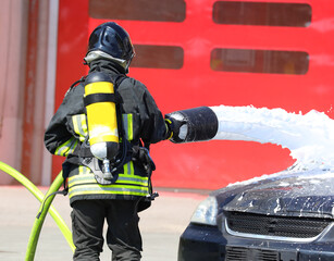 Fototapeta premium firefighter with big fire hose and white foam and a broken car