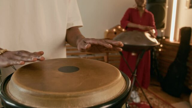 Hands of young unrecognizable African American male musician beating percussion while standing in front of camera in home studio during repetition with his girlfriend