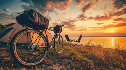 Bicycle with panniers near a beachside campsite with tent and camping chair under sunset sky