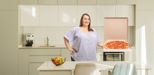 Overweight woman in a kitchen holding a pizza