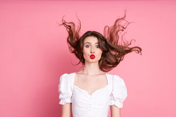Young woman with expressive red lips and flowing brown hair against a vibrant pink background, radiating charm and playfulness