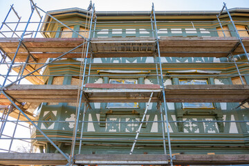 Renovation and repair. Scaffold on the facade of old house with green ornament.