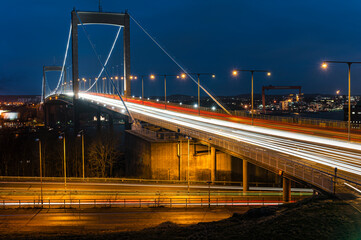 Naklejka premium Traffic flows across Älvsborgsbron bridge in Gothenburg during evening hours with illuminated vehicles and city lights