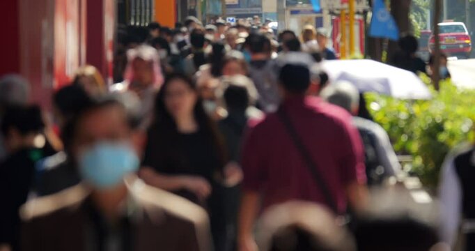 Defocused view of crowded Nathan Road sidewalk in Jordan, Hong Kong, with diverse pedestrians walking forward during busy urban moment. Blurred image ensures lack of recognizable faces