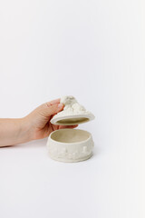 Hand opening white ceramic pot with frog lid