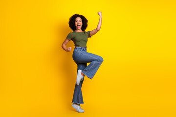 Happy young woman in casual outfit posing energetically on yellow background, expressing...
