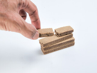 Obraz premium Hand Placing Wafer Cookies on a Stack with a White Background