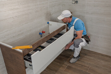 Installation of bathroom furniture. A worker hanging a bathroom cabinet on the wall.