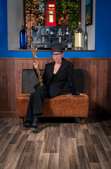 Young woman musician, holding a soprano saxophone in one hand seated on an armchair.