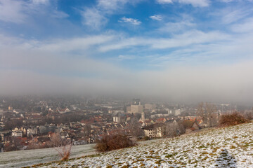 Panoramic view of St. Gallen, showing a city sprawling across a valley with distant hills, under a misty sky
