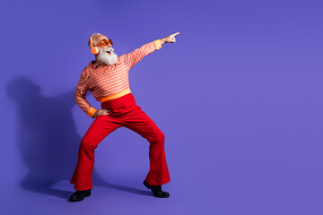 Energetic senior man in retro attire dancing against vibrant purple background with charismatic expression