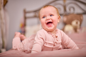 Fototapeta premium Joyful young female with light hair, caucasian ethnicity, in pink outfit on bed. Warm lighting enhances cheerful expression. Plush decor adds cozy touch