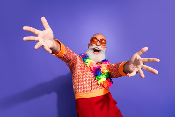 Eccentric senior man in retro inspired fashion poses with outstretched arms against purple...