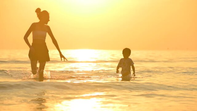 Golden Shoreline: A silhouetted mother and child frolic in the tranquil surf during a warm, sun-kissed morning, creating a heartwarming scene of familial bliss.