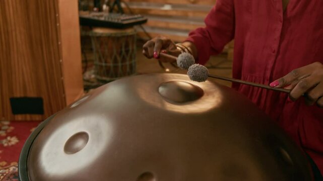 Hands of young unrecognizable African American female musician using drumsticks to beat metallic surface of ethnic glucophone while creating and recording new music