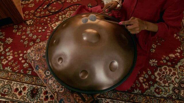High angle of young unrecognizable African American woman in magenta dress sitting on carpet in home studio and playing glucophone while creating new sounds