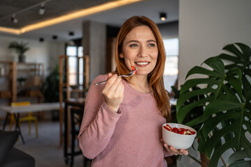 Happy woman eating strawberries at home in modern apartment
