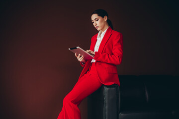 Confident Female Professional in Red Suit Using Digital Tablet Against Dark Background