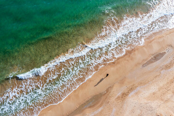 Aerial drone overhead view of beautiful waves and alone human with big shadow on sand.