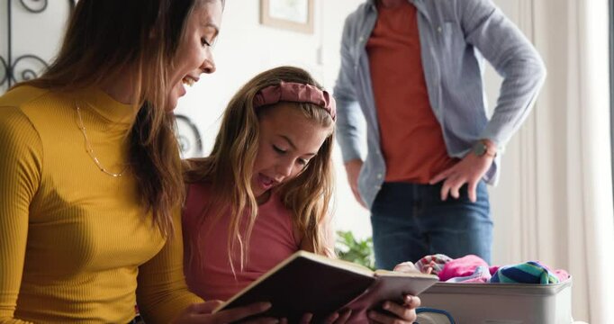 Diverse family sharing hug and packing suitcase after daughter showing tablet pages in bedroom