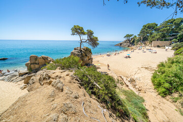 Tourists relaxing on sandy beach at picturesque cala cap roig in costa brava, spain