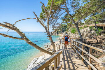 Tourists walking on wooden footbridge near beautiful sandy beach in costa brava, catalonia
