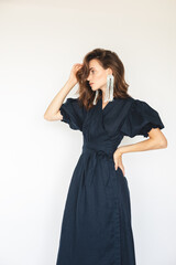 Attractive brunette woman wear navy blue dress with long cuffed puff sleeves and silver beads earrings. Sexy brunette woman with curly short hair look sensual, fix her hair