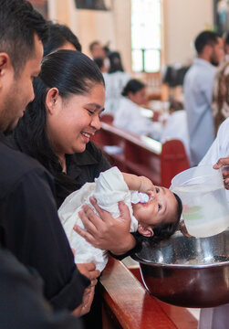 An Indonesian baby is baptized with water in a church while held by her mother. A sacred and emotional moment during a Christian baptism surrounded by family and tradition.