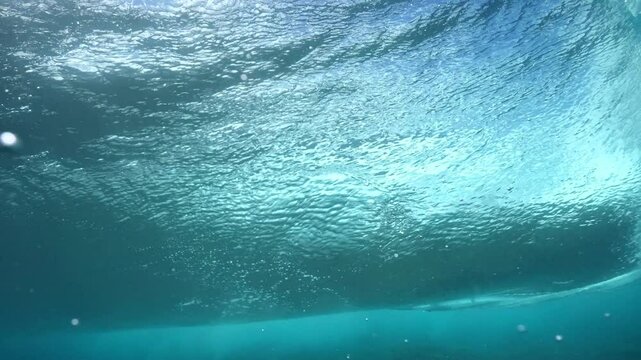 Underwater shot of blue barreling wave with silhouette of surfer in the barrel riding in slow motion. Tahiti famous surf destination for surfers, French Polynesia. 