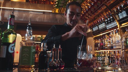 Smart Asian bartender using stirring mixed alcohol syrup into glass with ice for on the rock served mixing looking camera zoom out special refresh cocktail nightlife mixology at nightclub. Vinosity.