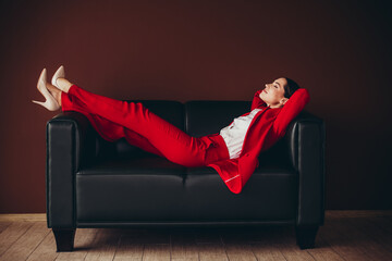 Attractive Confident Businesswoman Relaxing on a Sofa in Elegant Red Suit in Modern Office