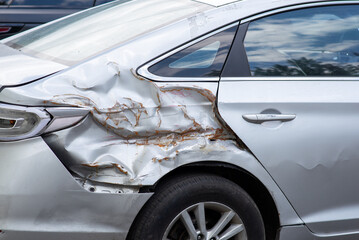 Damaged car rear side with severe dents and rust, showing aftermath of a collision or accident.