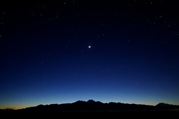Starry night sky with crescent moon over mountain silhouette landscape