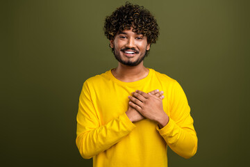 Smiling young man in yellow shirt with hand gesture conveying gratitude against khaki green studio...