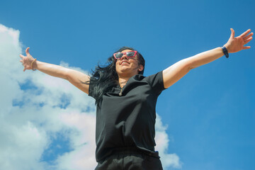 Young woman opening arms enjoying freedom and success under blue sky