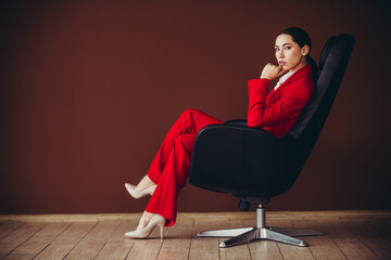 Stunning Professional Young Woman in Red Suit Sitting Confidently in Modern Armchair